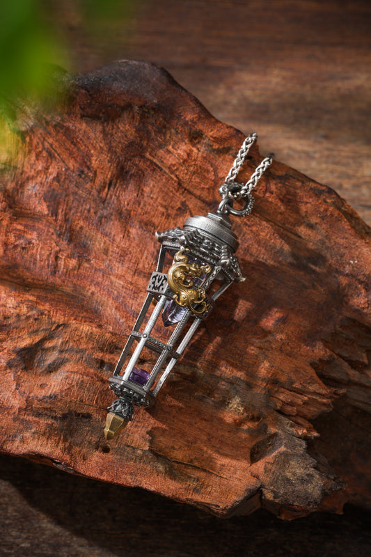 An elongated pavilion-shaped pendant containing purple crystal, with a chain passing through its top fitting, on textured brown wood.